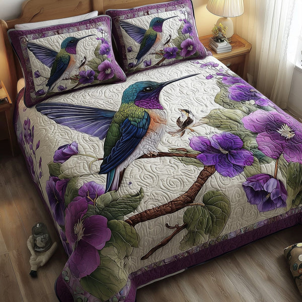 Purple Hummingbird Dancing quilted 3-piece bedding set on a made bed with two matching pillow shams